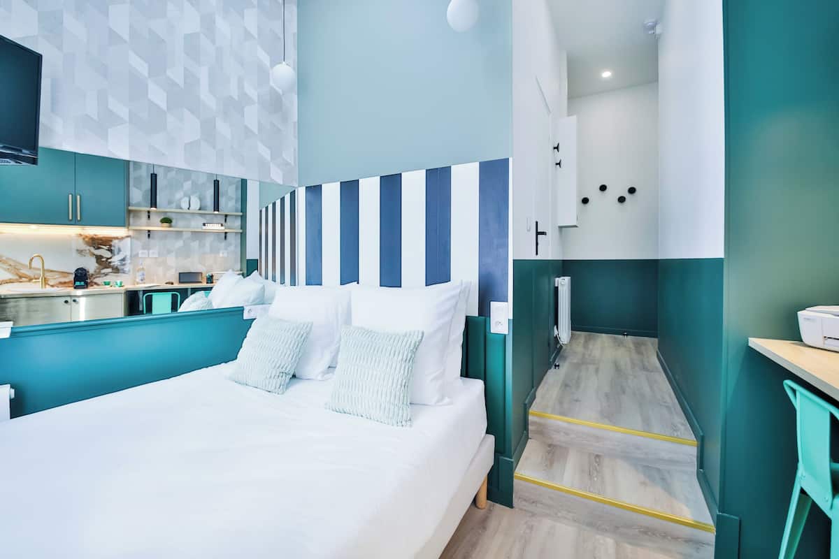 A modern hotel room with a large bed, a kitchenette, and a bathroom.