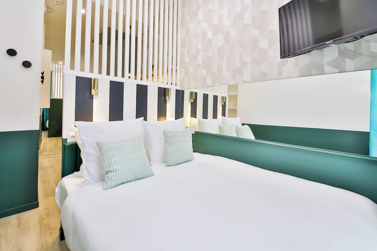 A modern hotel room with a large bed, a green headboard, and a flat-screen TV mounted on the wall.