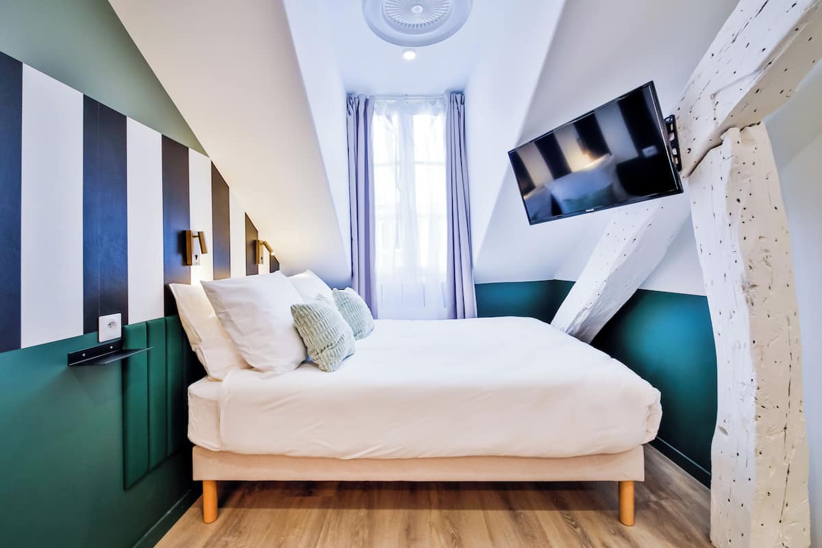 A modern hotel room with a large bed, a flat-screen TV mounted on the wall, and a view of the city through the window.
