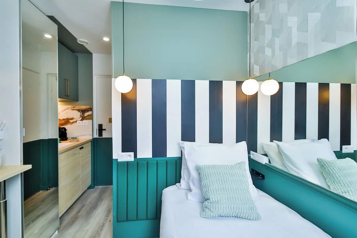 A modern hotel room with a teal accent wall, a striped headboard, and a large mirror.