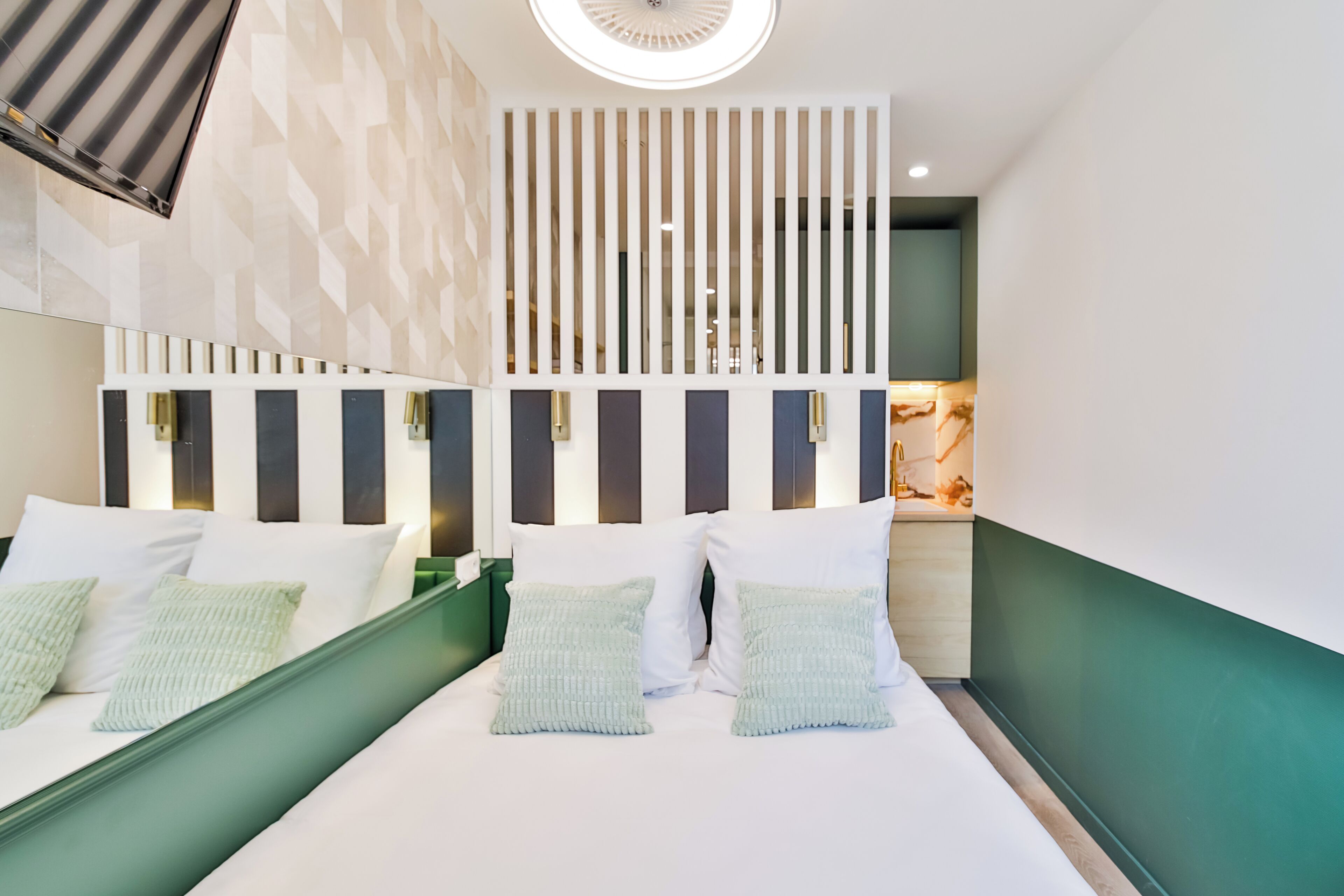 Habitación de hotel moderna con una cama grande, paredes de acento verde y un separador decorativo con listones verticales.