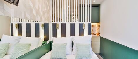Habitación de hotel moderna con una cama grande, paredes de acento verde y un separador decorativo con listones verticales.