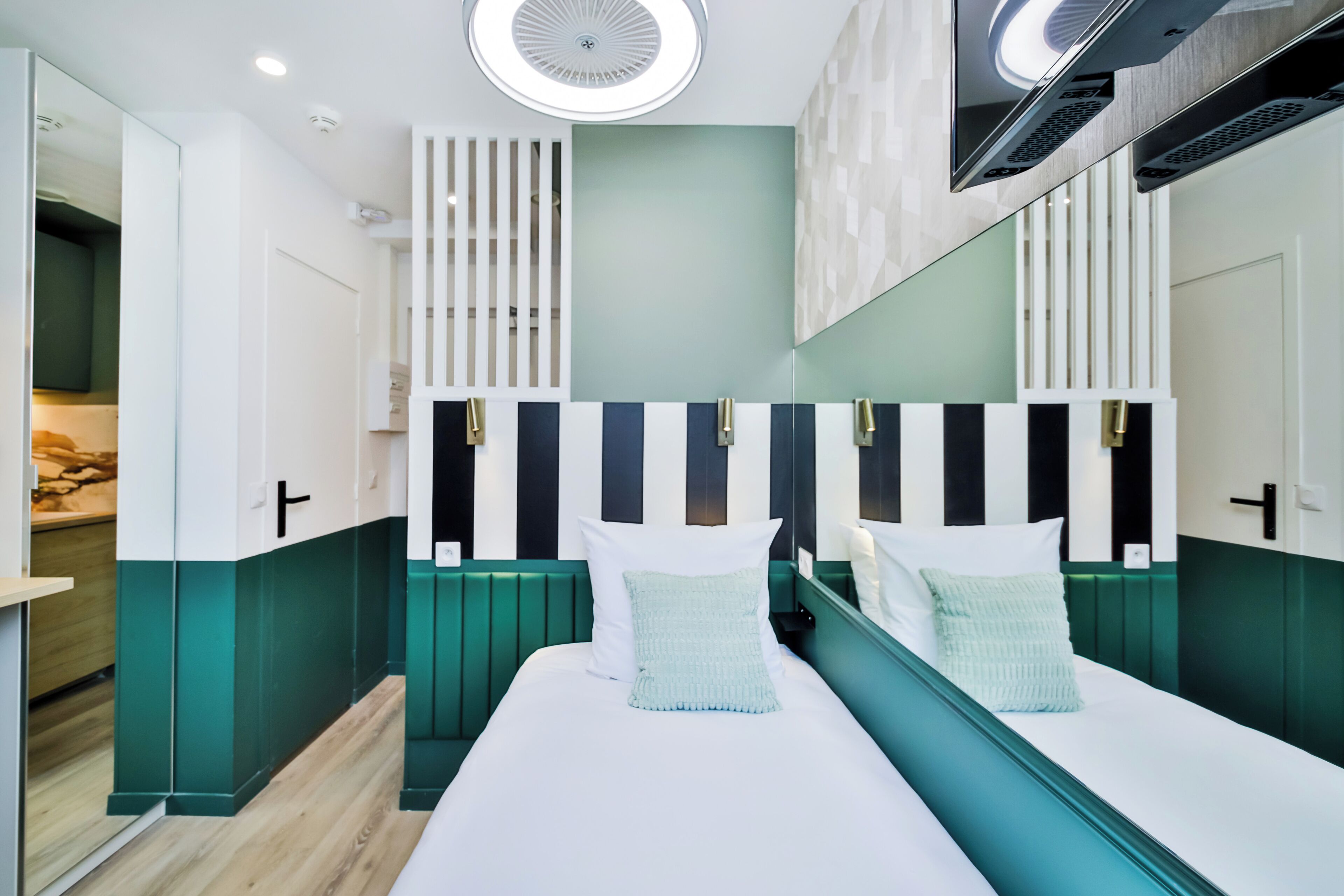 Een moderne hotelkamer met een groot bed, een kleurenschema in groen en wit, en een grote spiegel boven het bed.