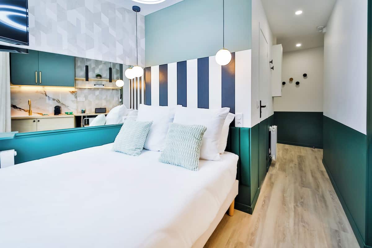 A modern hotel room with a large bed, a kitchen area, and a bathroom.