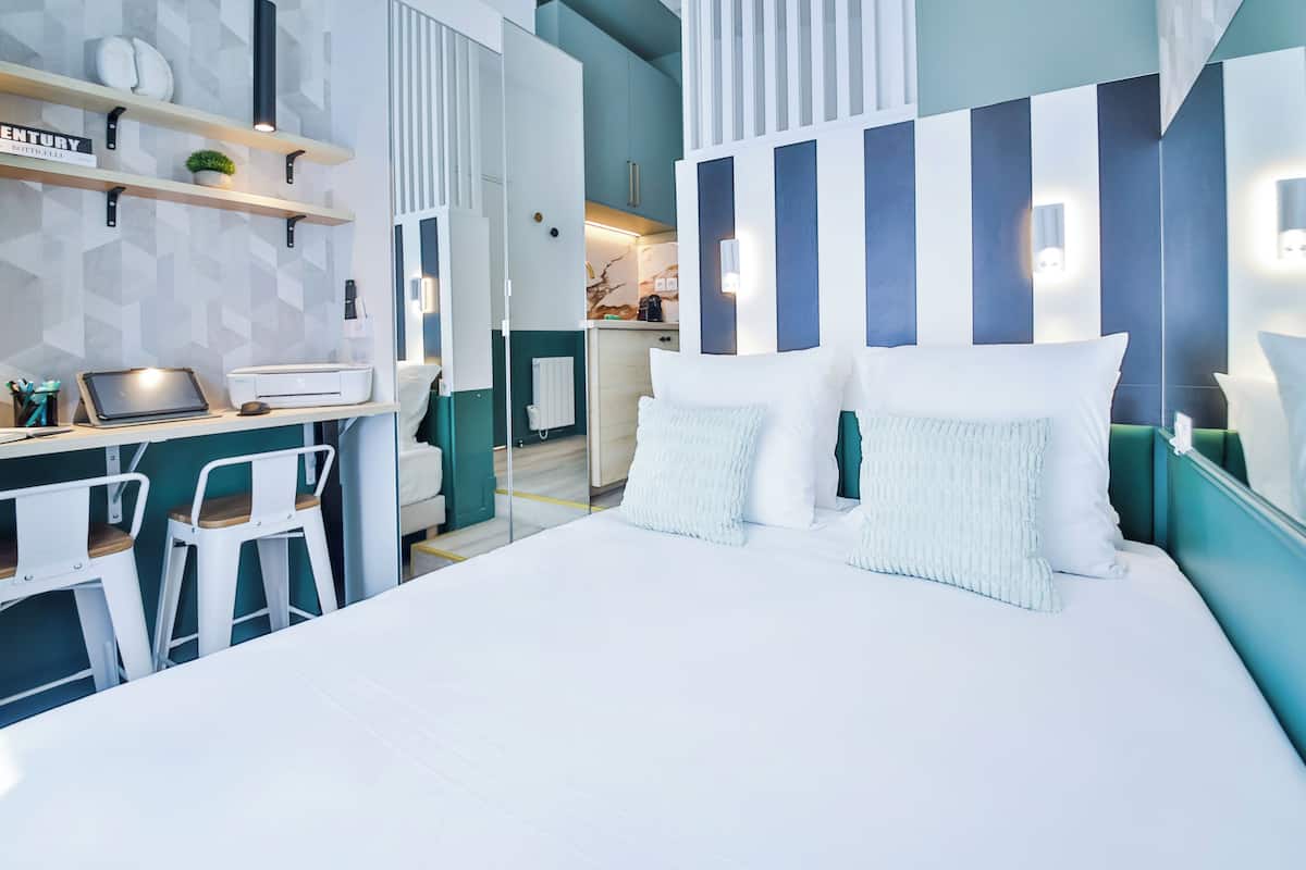 A modern hotel room with a large bed, a desk with a laptop, and a seating area with chairs.