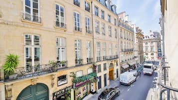 Une vue d’une rue, montrant un immeuble à plusieurs étages, avec un café au rez-de-chaussée, un restaurant doté d’une terrasse et une entrée bien visible.