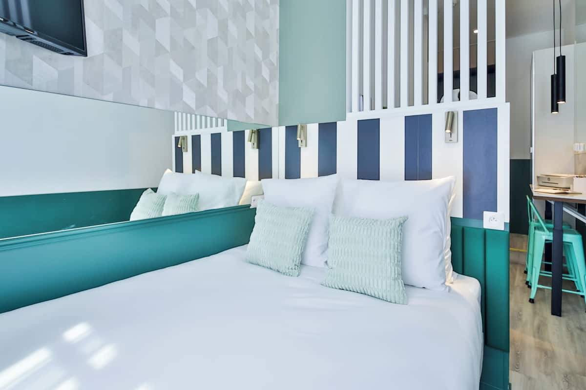 A modern hotel room with a large bed, a desk, and a TV mounted on the wall.
