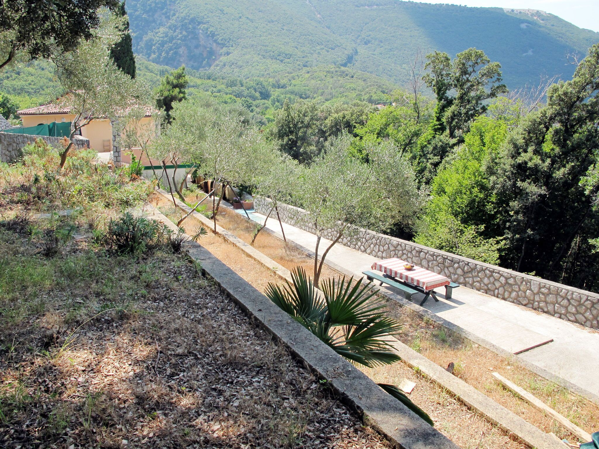 Un sentier bordé d’un muret et agrémenté d’un banc, qui mène à un bâtiment doté d’un toit en tuiles.