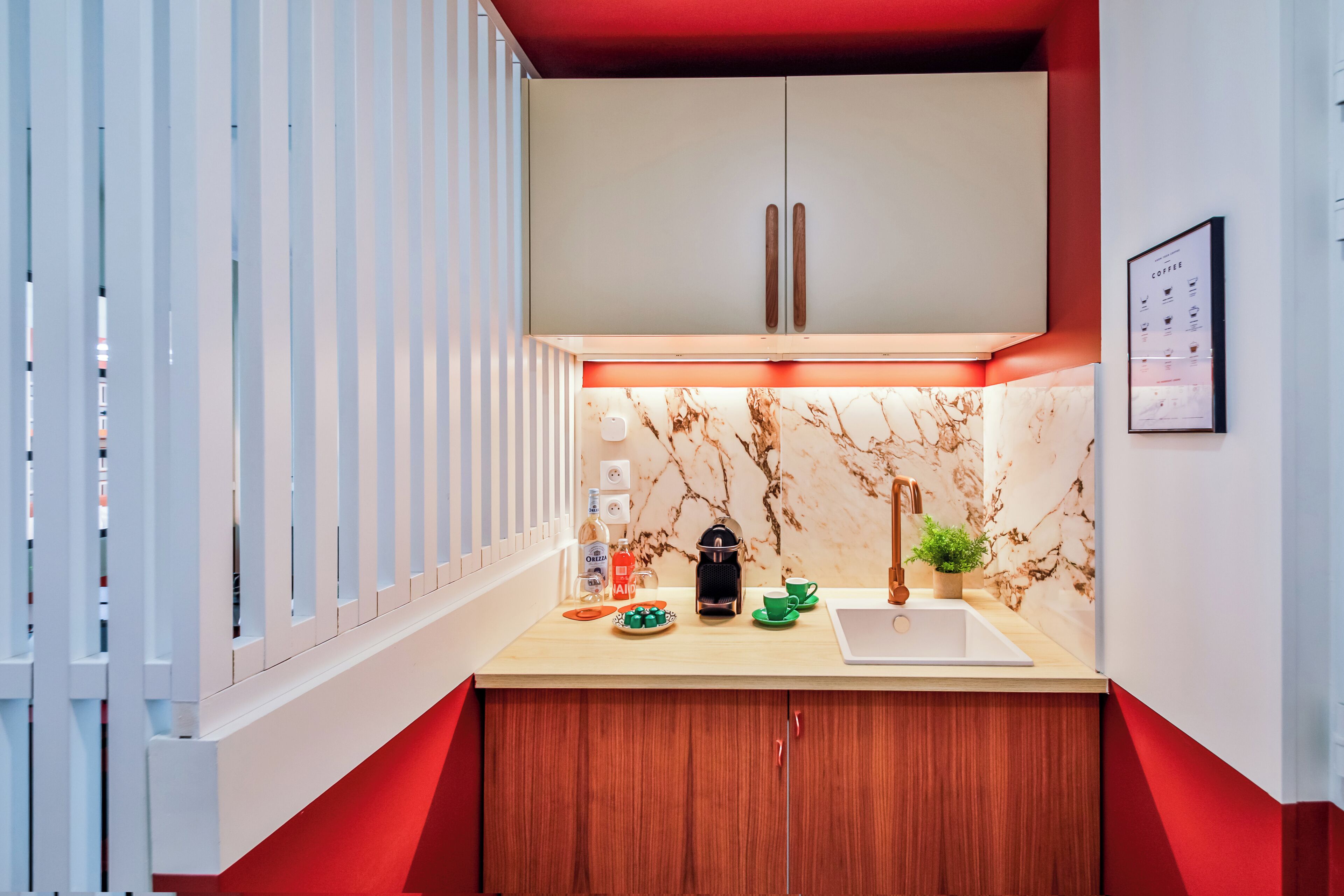 Una cucina moderna con zoccolo in marmo, mobili in legno e una parete di accento rossa.