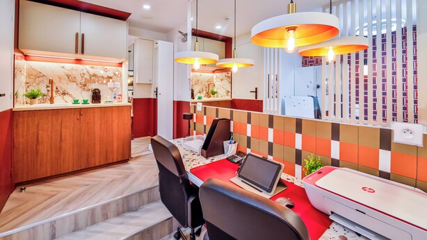 Une cuisine moderne avec des plans de travail en marbre, un coin repas avec une table rouge et une imprimante posée sur la table.
