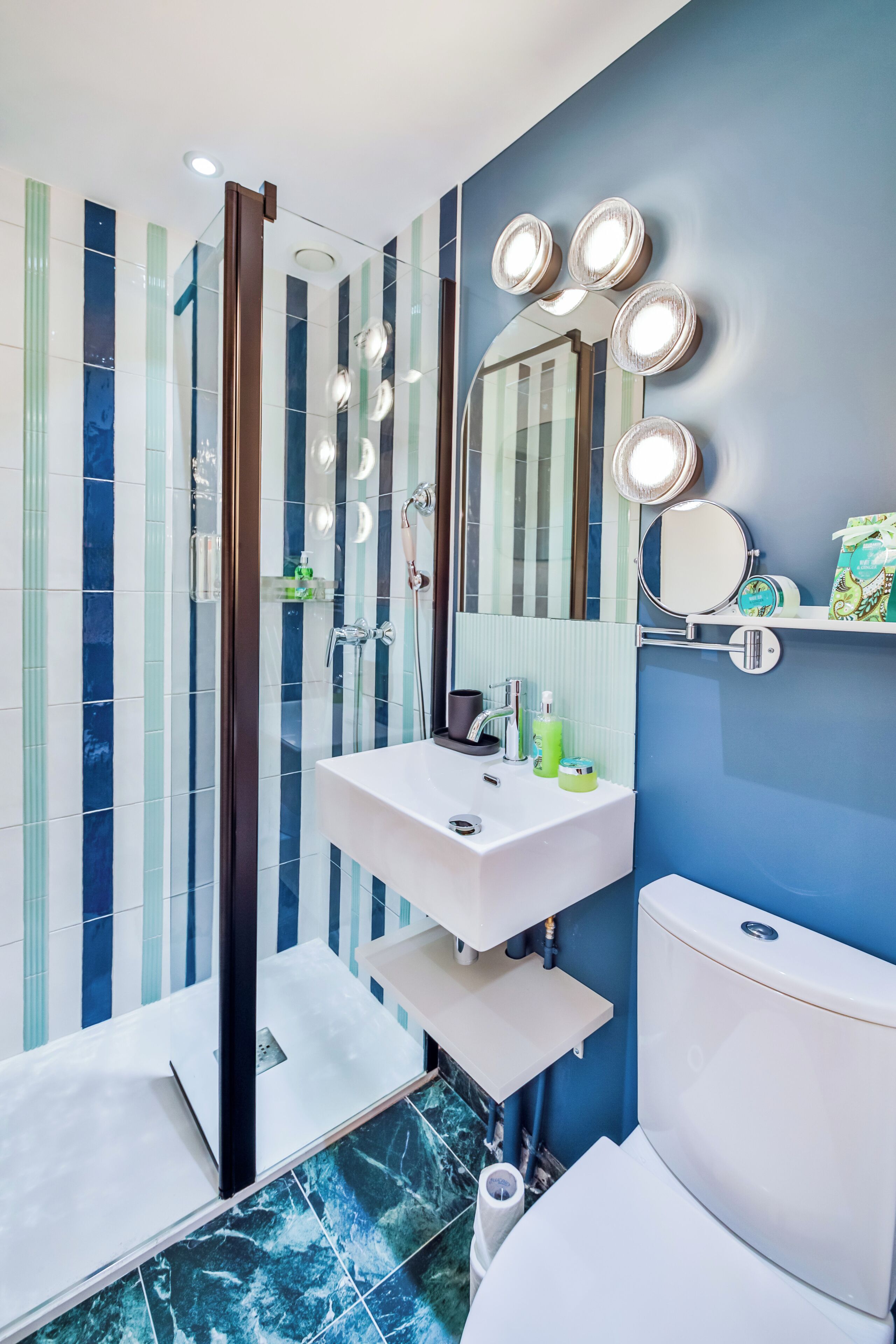 A modern bathroom with a glass shower enclosure, a white sink, and a large mirror with lights.