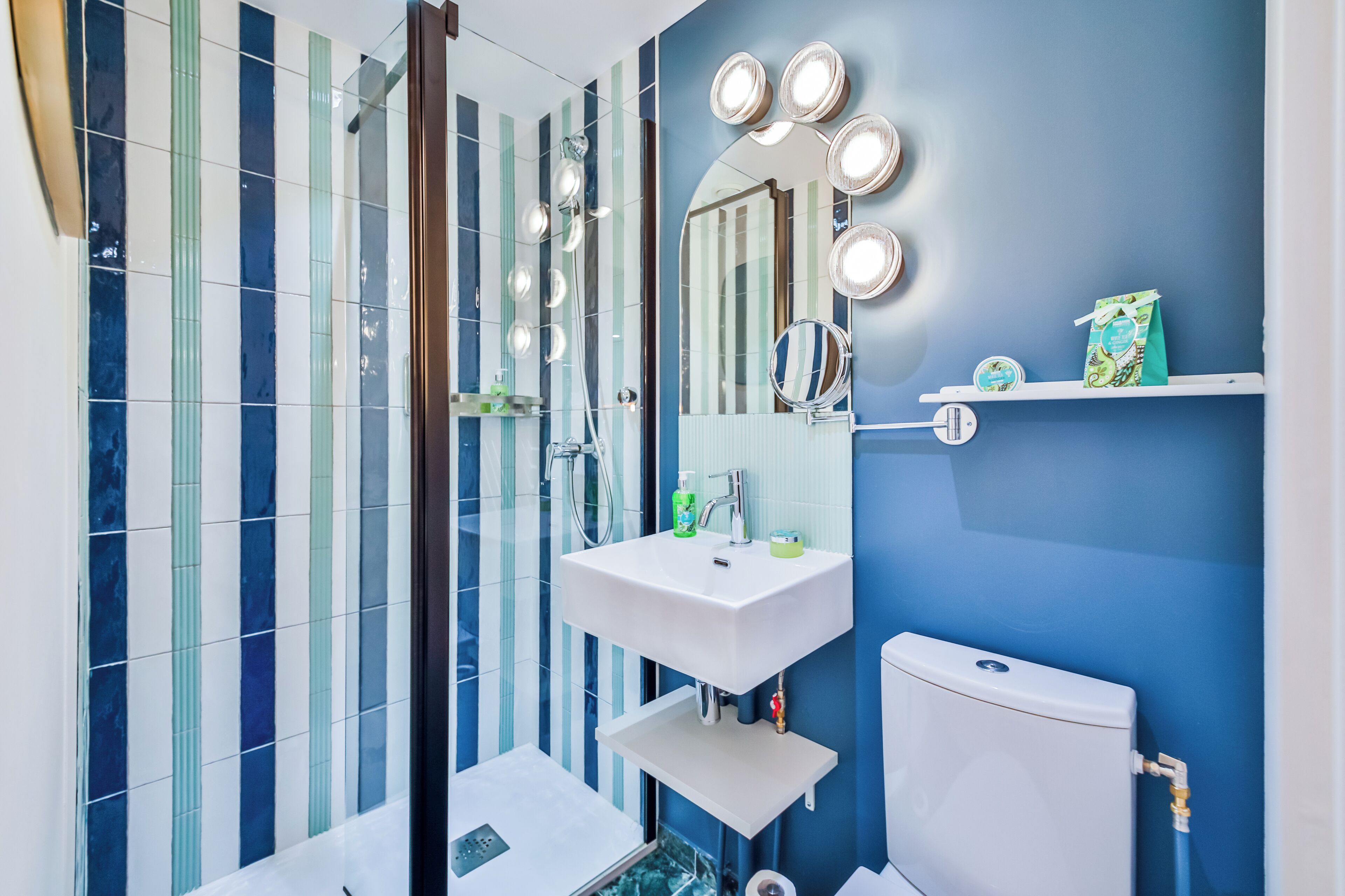 Een badkamer met een wit wastafel, spiegel en toilet, blauwe wanden en gestreepte tegels.