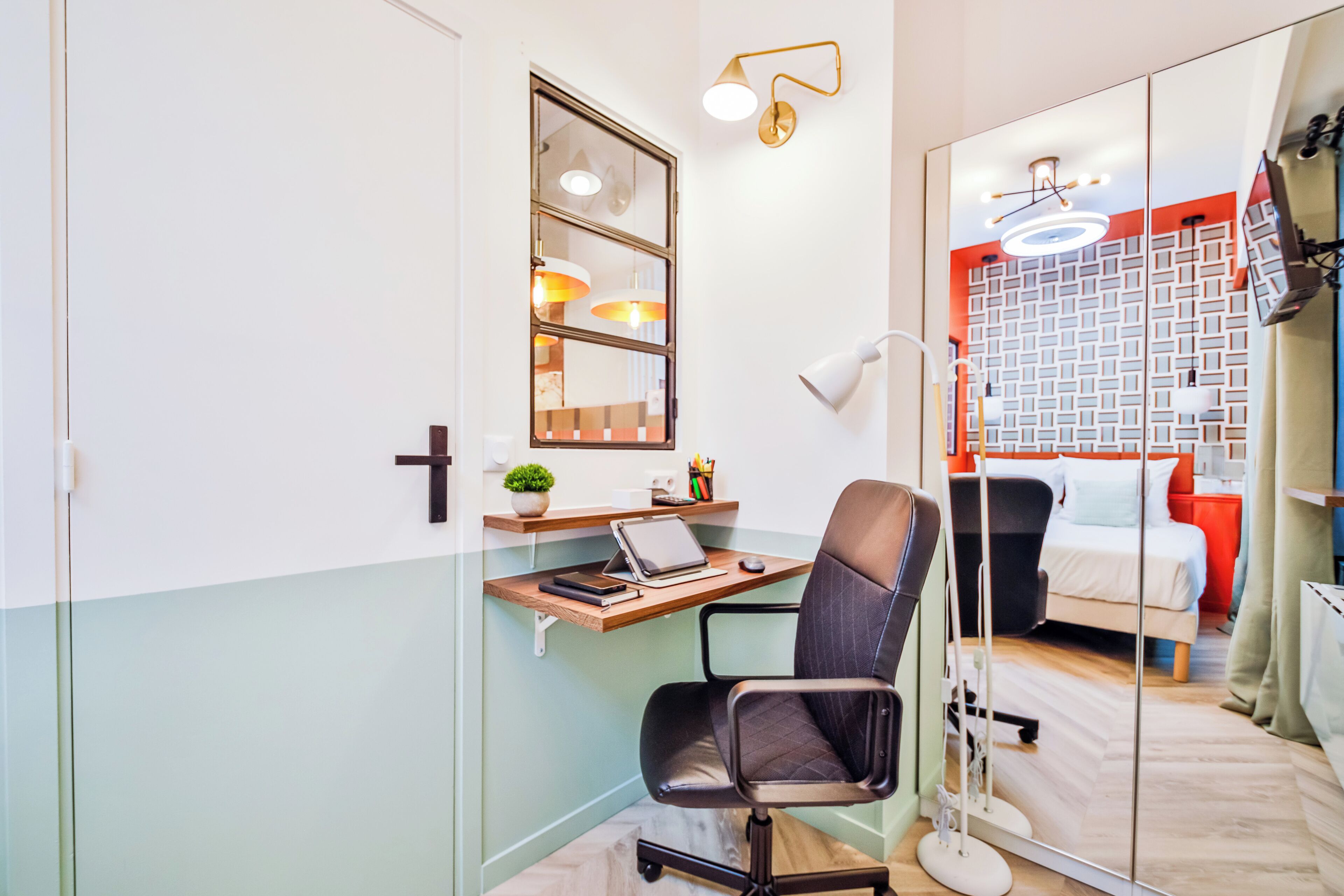 Een moderne slaapkamer met een bed, een bureau met een laptop, een stoel en een nachtkastje met een lamp.