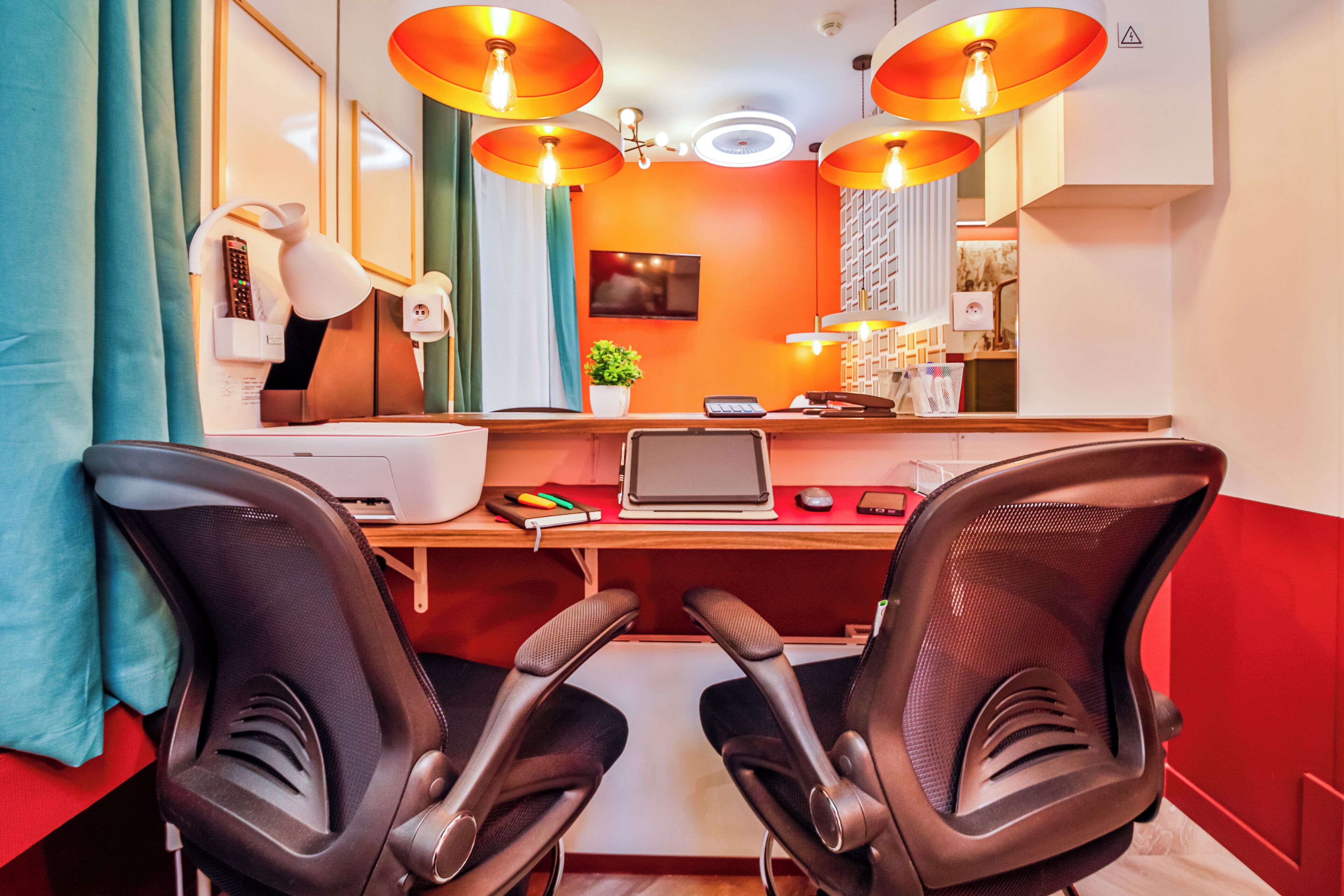 A modern office space with two black office chairs, a wooden desk with a laptop, a printer, and a small plant.