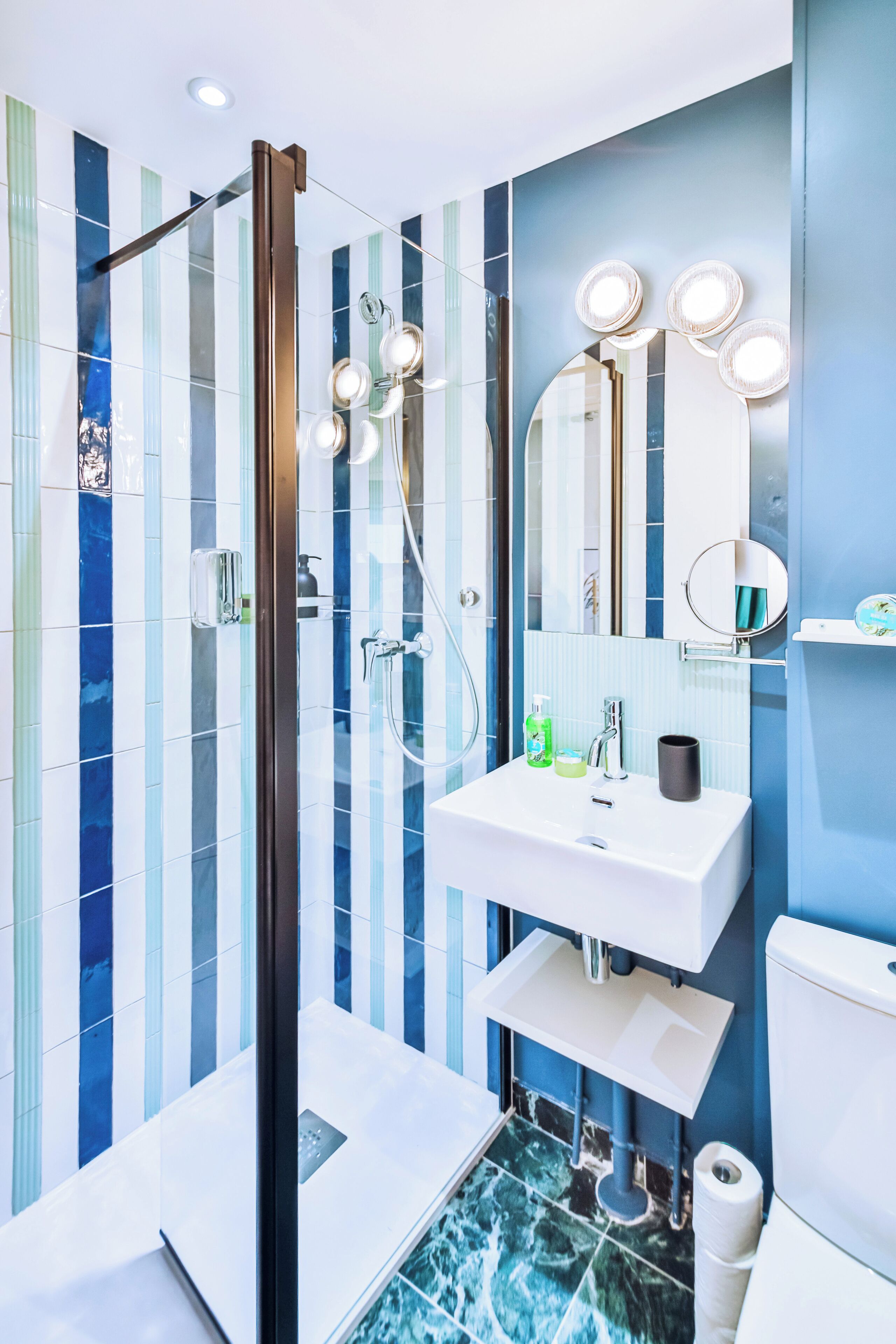 A modern bathroom with a glass shower enclosure, a white sink with a mirror above it, and a blue-tiled wall.