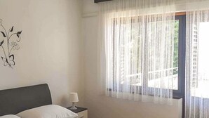 A neatly made bed with pillows, a nightstand with a lamp, and a window with sheer curtains. - Apartment Monja by Interhome (Novi Vinodolski)