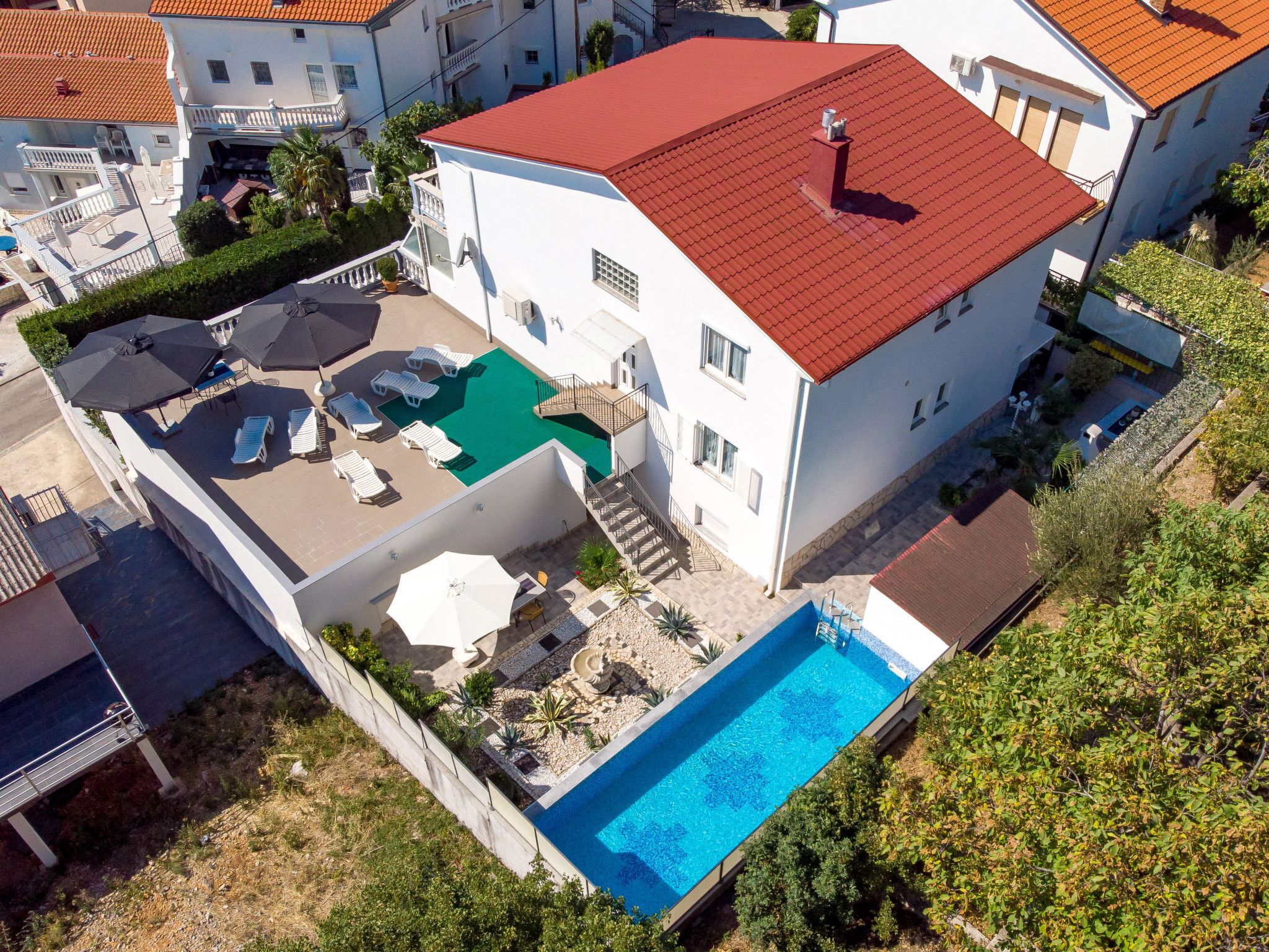 Un bâtiment à deux étages, doté d’un toit rouge, d’une piscine et d’un espace extérieur aménagé avec des parasols.
