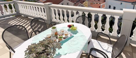 Una terraza con mesa dispuesta para tomar té, rodeada de sillas, con vistas a un pueblo costero.