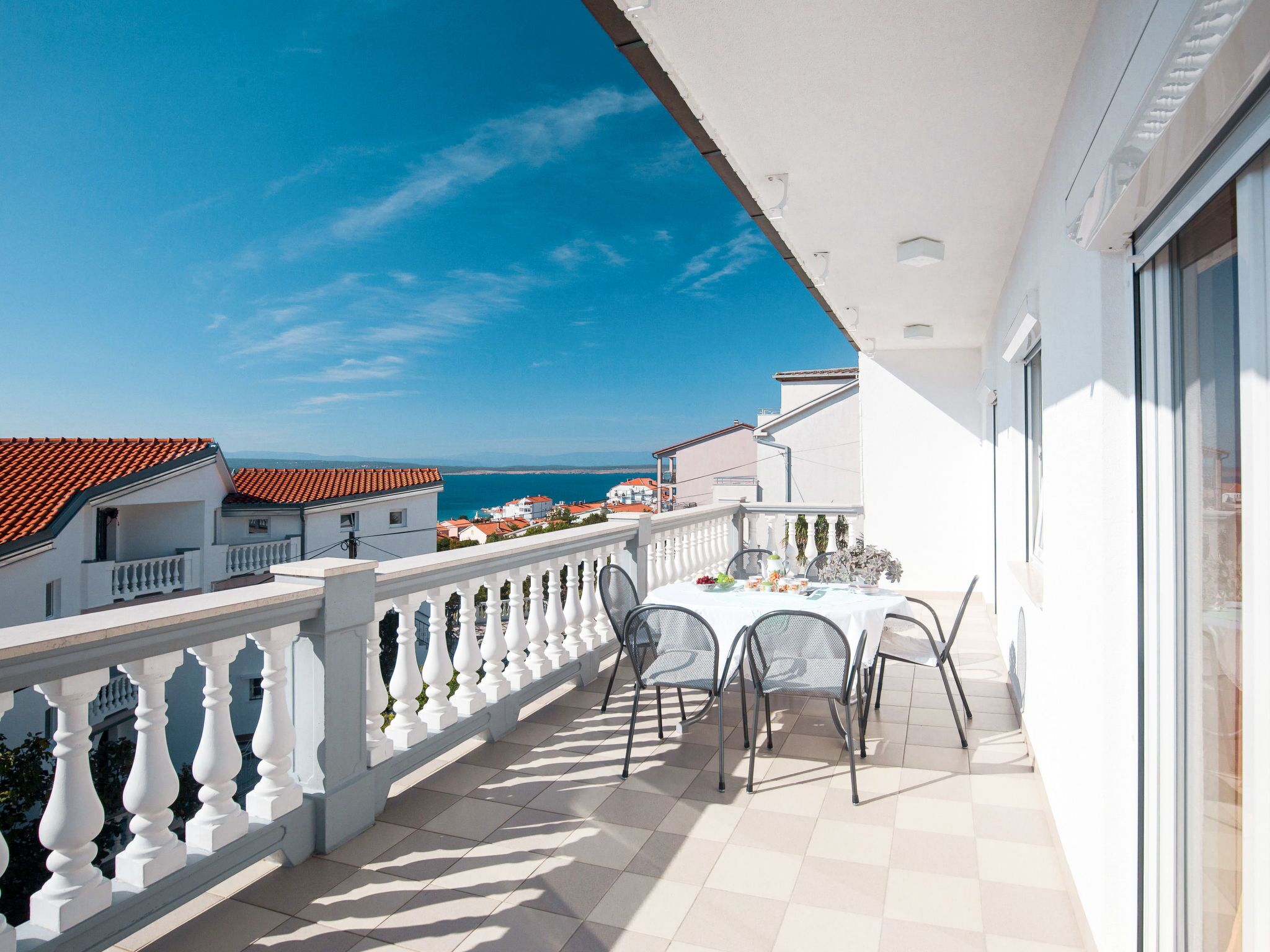 A balcony with a table set for dining, overlooking a coastal area with buildings and the sea.