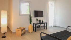 Una habitación moderna y luminosa, con una cama, un televisor montado en la pared, una mesita con plantas y una ventana con cortinas.