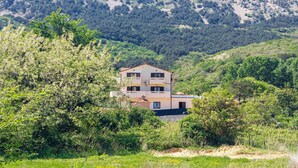 A two-story building with a flat roof, surrounded by dense greenery and mountains in the background. - Apartment Marija by Interhome (Krk/Baška)
