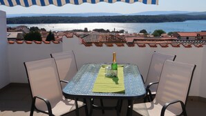 Mesa con sillas bajo un toldo a rayas, con vista a un lago y un pueblo.