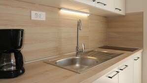 Una cocina moderna con un lavamanos de acero inoxidable, una cafetera y armarios blancos.