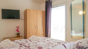 Un dormitorio con cama, armario de madera, televisor montado en la pared, orquídea en maceta y ventana con cortinas.