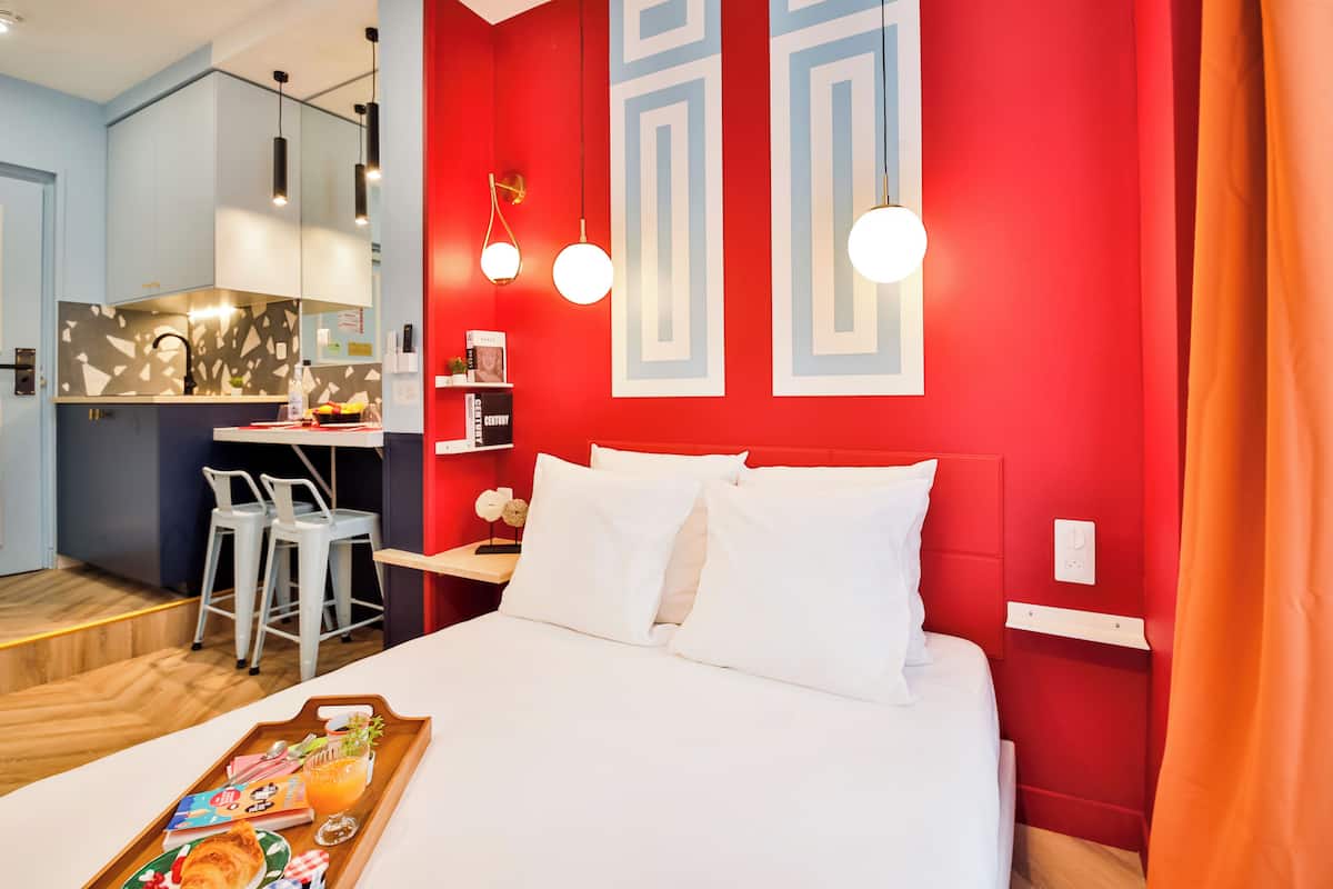 Un cuarto de hotel moderno con una pared roja decorativa, una cama blanca y una bandeja de desayuno sobre la mesita de noche.