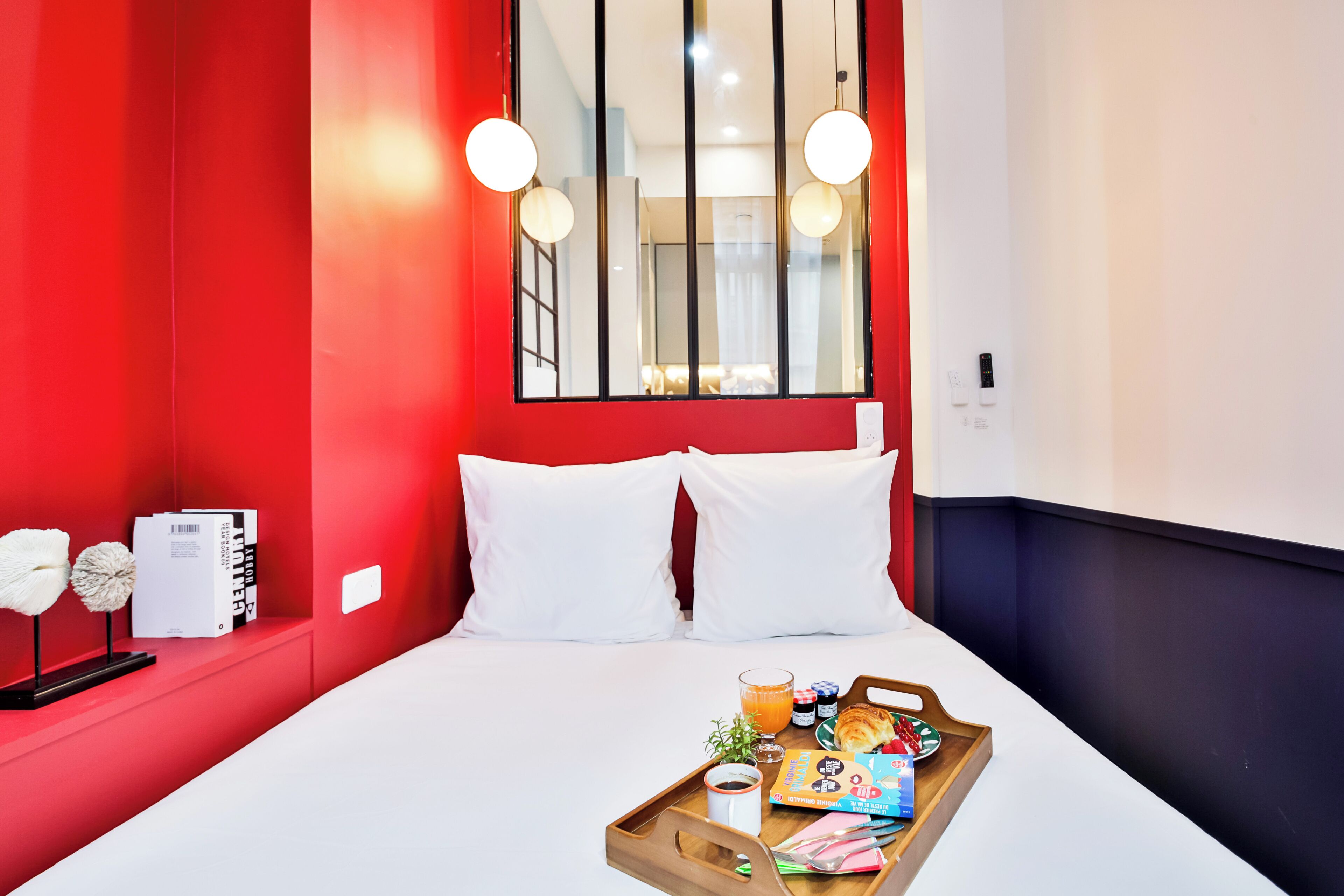 A hotel room with a red accent wall, a large window, a bed with white bedding, and a breakfast tray on the bed.