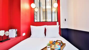 A hotel room with a red accent wall, a large window, a bed with white bedding, and a breakfast tray on the bed.