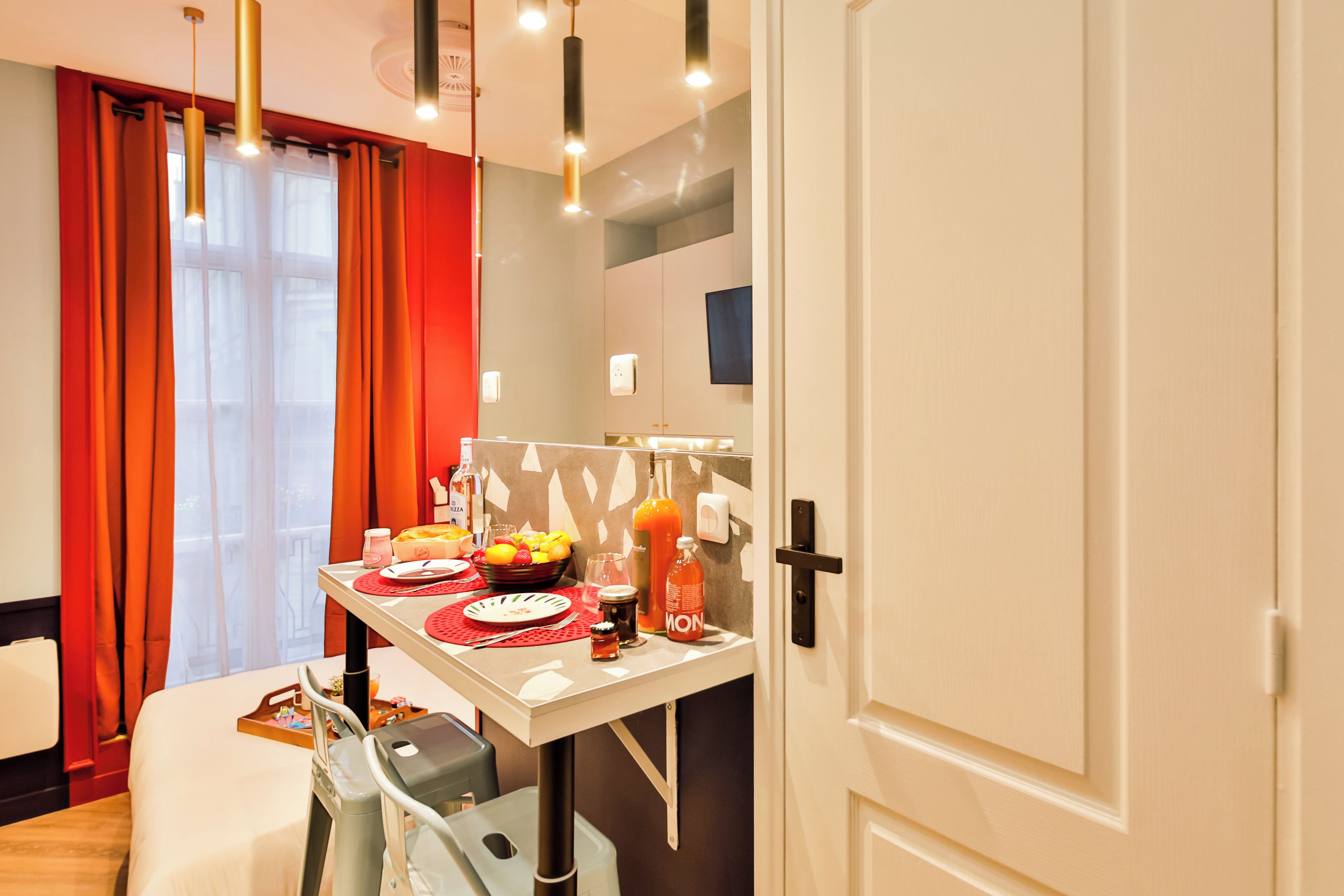 A hotel room with a dining table set for breakfast, a bed, a suitcase, and a door.