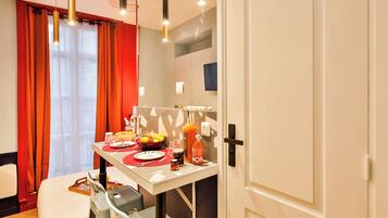 A hotel room with a dining table set for breakfast, a bed, a suitcase, and a door.