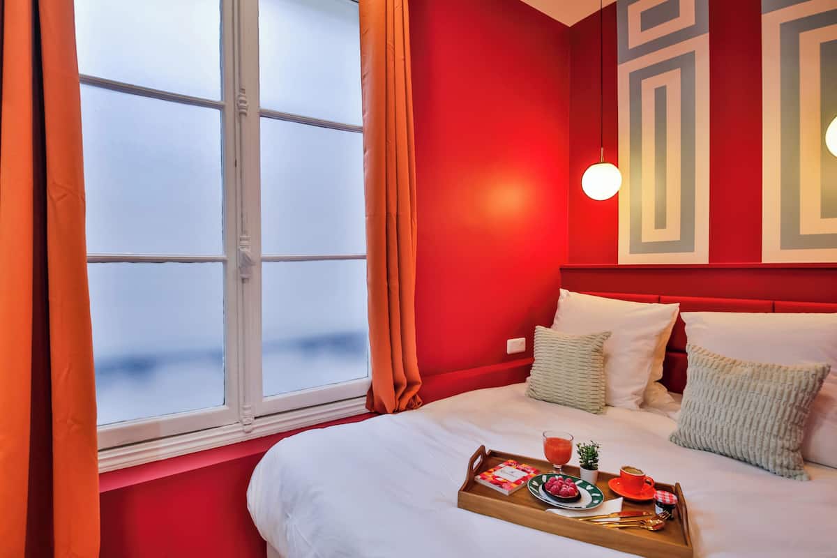 Habitación de hotel con una cama grande, paredes rojas y una ventana con cortinas.