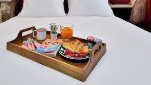 A hotel room with a red accent wall, a wooden bedside table with a tray of breakfast, white bedding, and a bookshelf. - WS Louvre - Saint-Roch (Paris)
