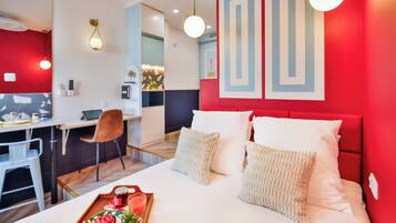 A modern hotel room with a red accent wall, a bed with white bedding, a desk with a chair, and a tray with food and drink.