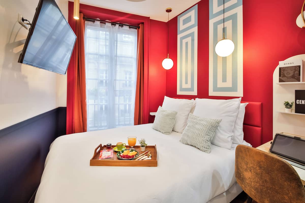 Una habitación de hotel con cama, bandeja de desayuno y televisor montado en la pared.