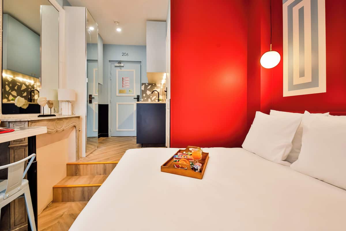 Habitación de hotel con cama, bandeja de desayuno, escritorio y espejo.