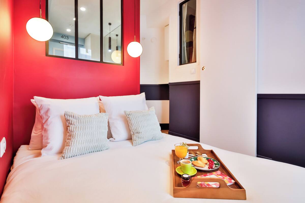 Una habitación de hotel con una cama, una bandeja con alimentos para el desayuno y una pared roja.