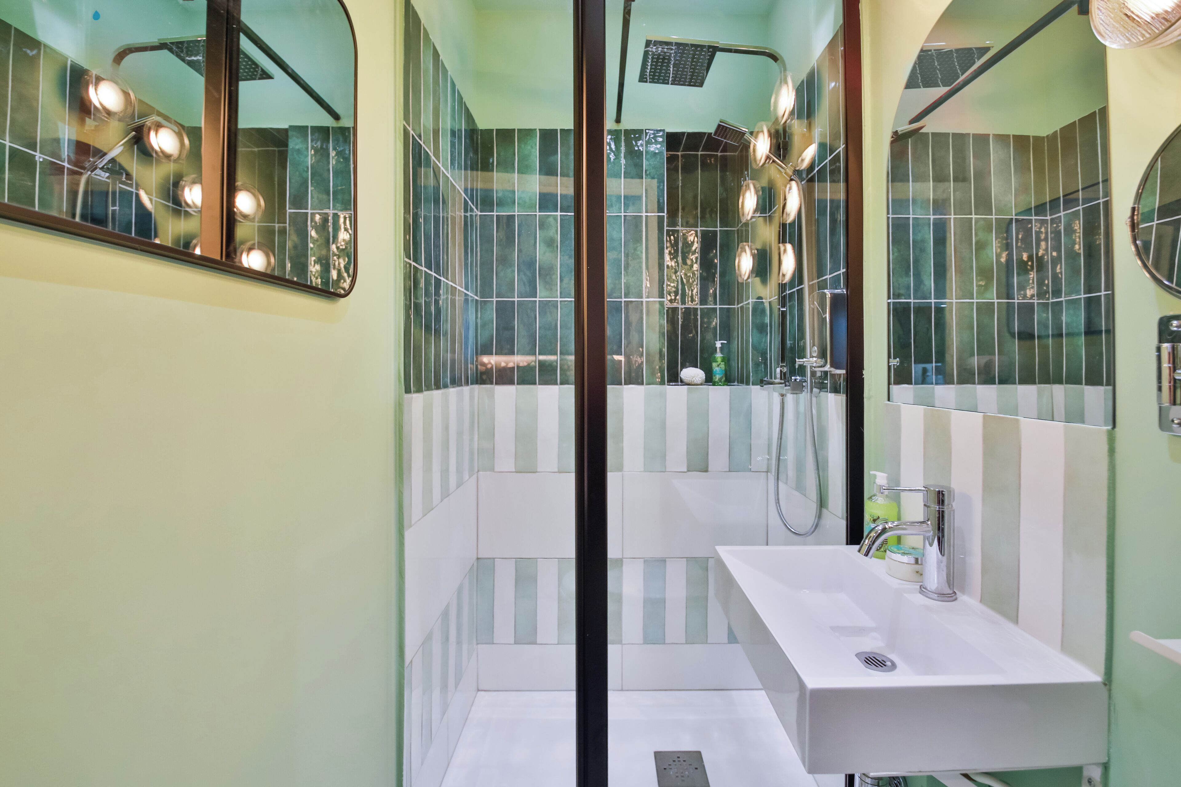 Une salle de bain moderne avec un grand miroir, un lavabo blanc et un espace douche.