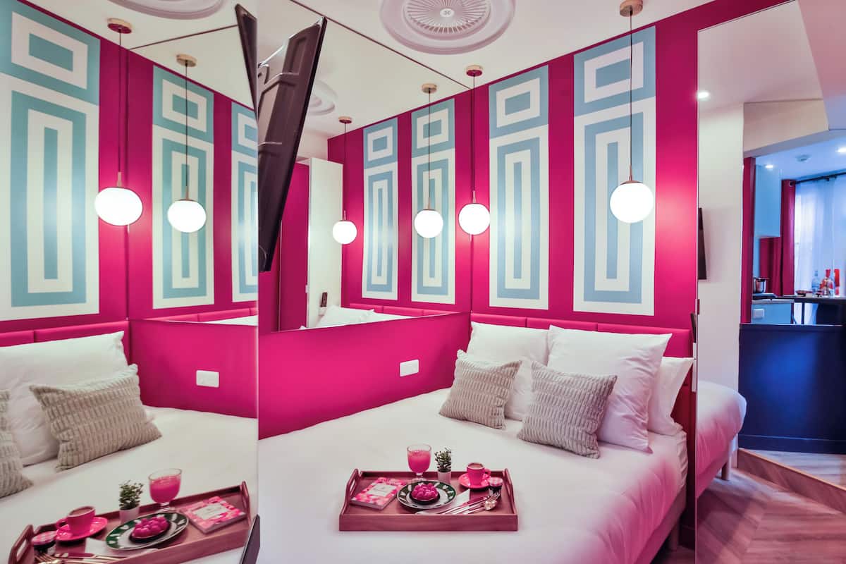 Una habitación de hotel moderna con una paleta de colores rosa intenso y turquesa, una cama grande con ropa blanca y una bandeja de desayuno sobre la cama.
