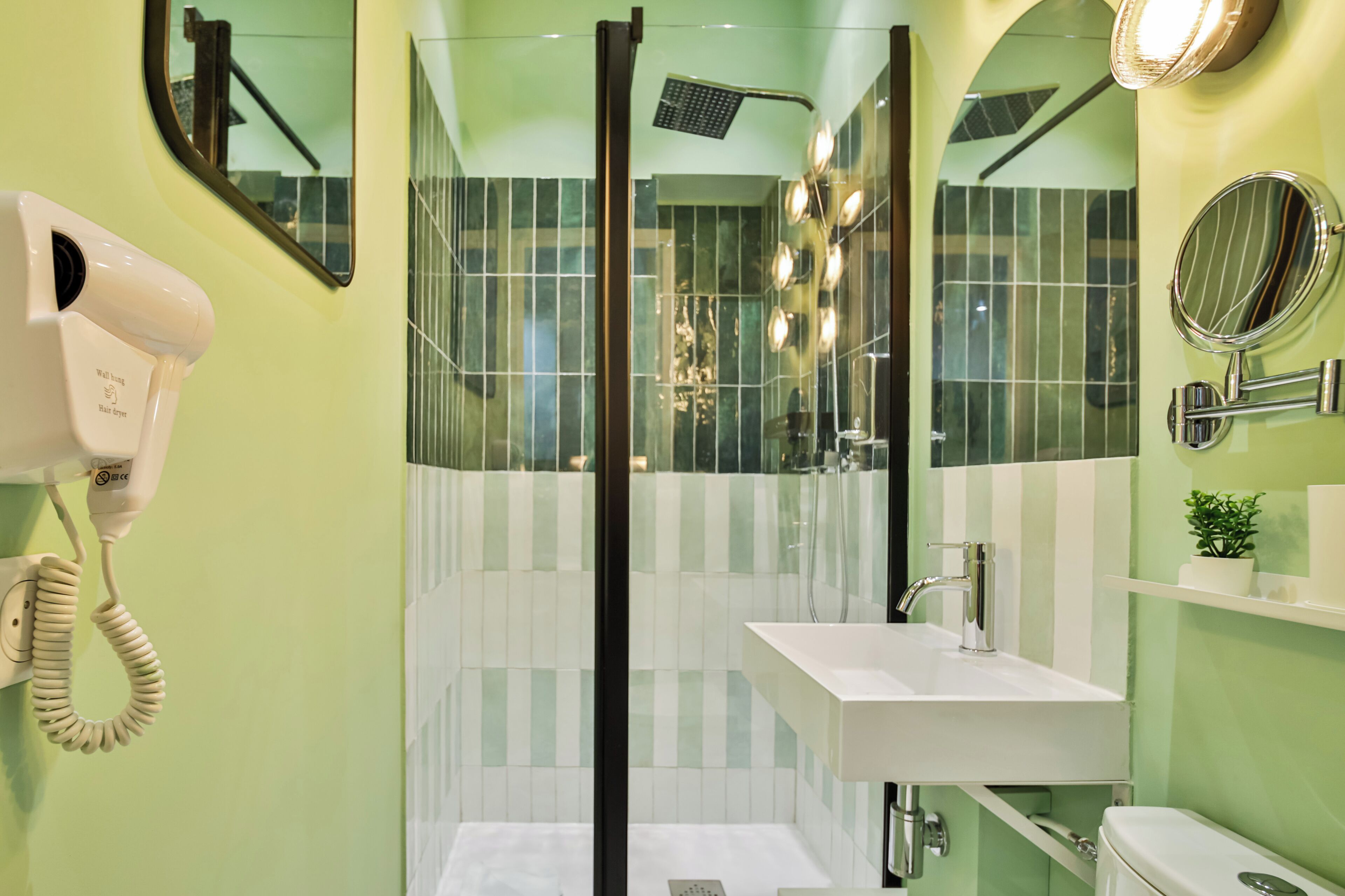A bathroom with a glass-enclosed shower, a white sink, and a hairdryer mounted on the wall.