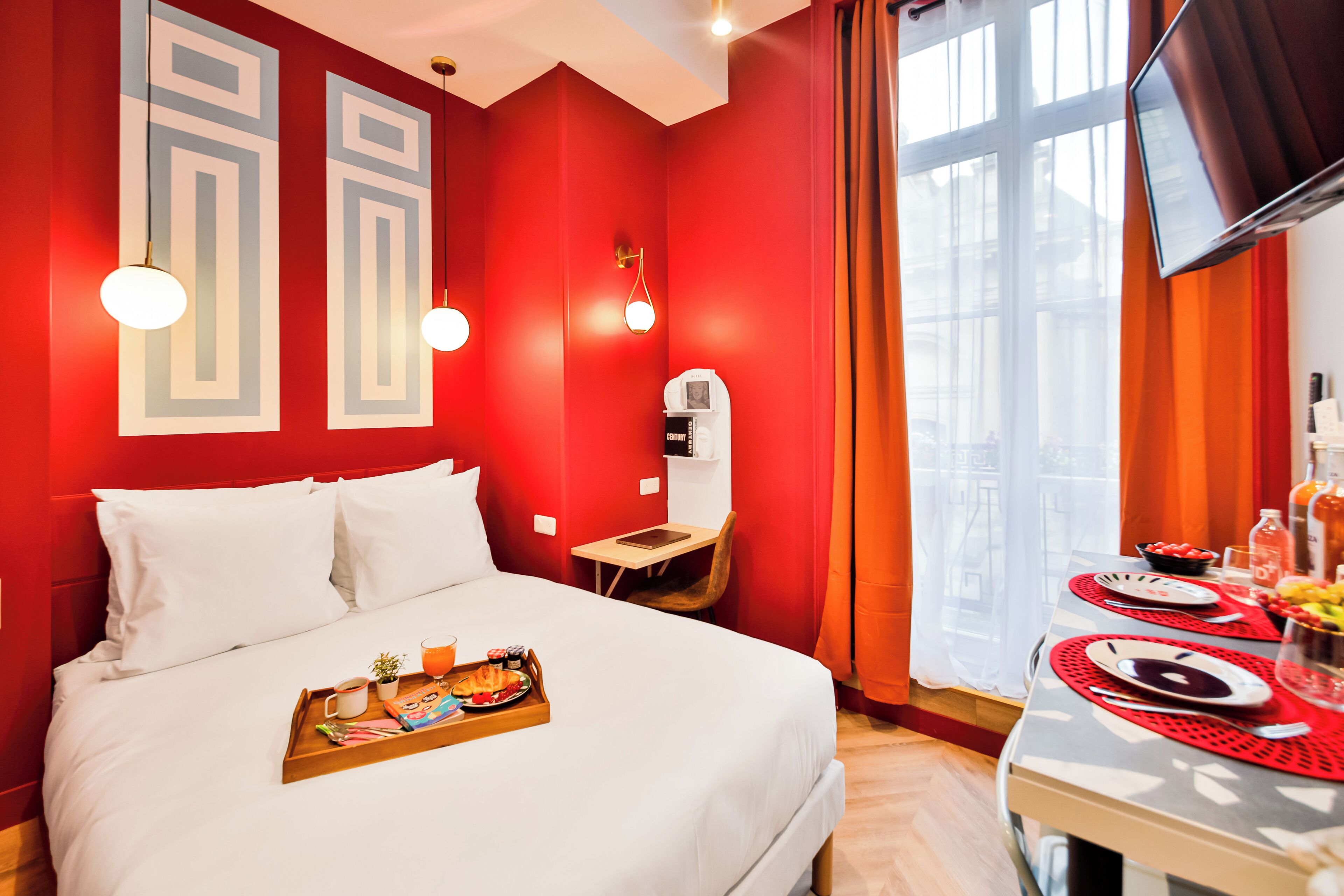 Hotellihuone, jossa on suuri sänky, työpöytä tuolilla, televisio ja aamiaistarjoilu sängyllä.