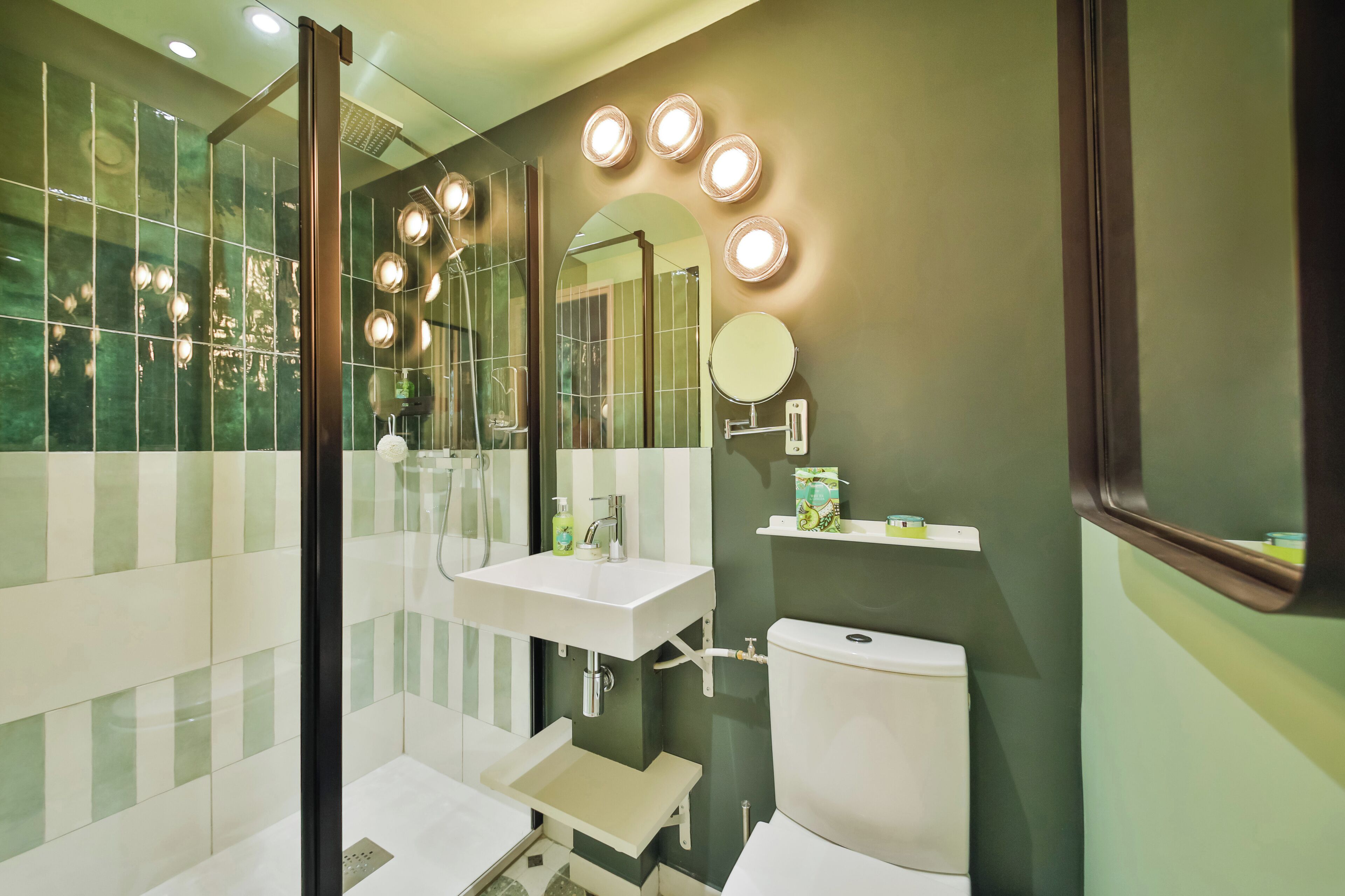 Une salle de bain moderne avec une douche à parois de verre, un lavabo blanc, des toilettes et un miroir de coiffeuse avec éclairage.