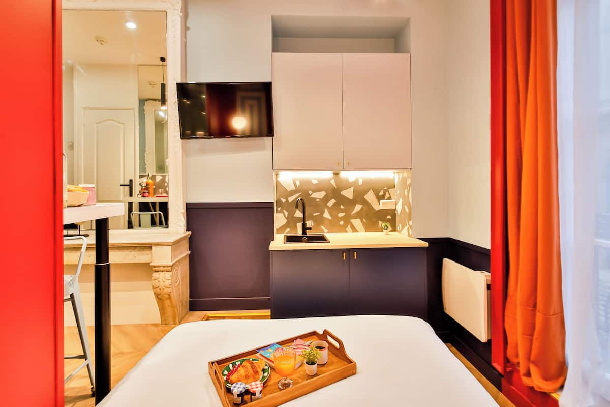 Habitación de hotel con cama, bandeja de desayuno, televisor y una pequeña kitchenette.