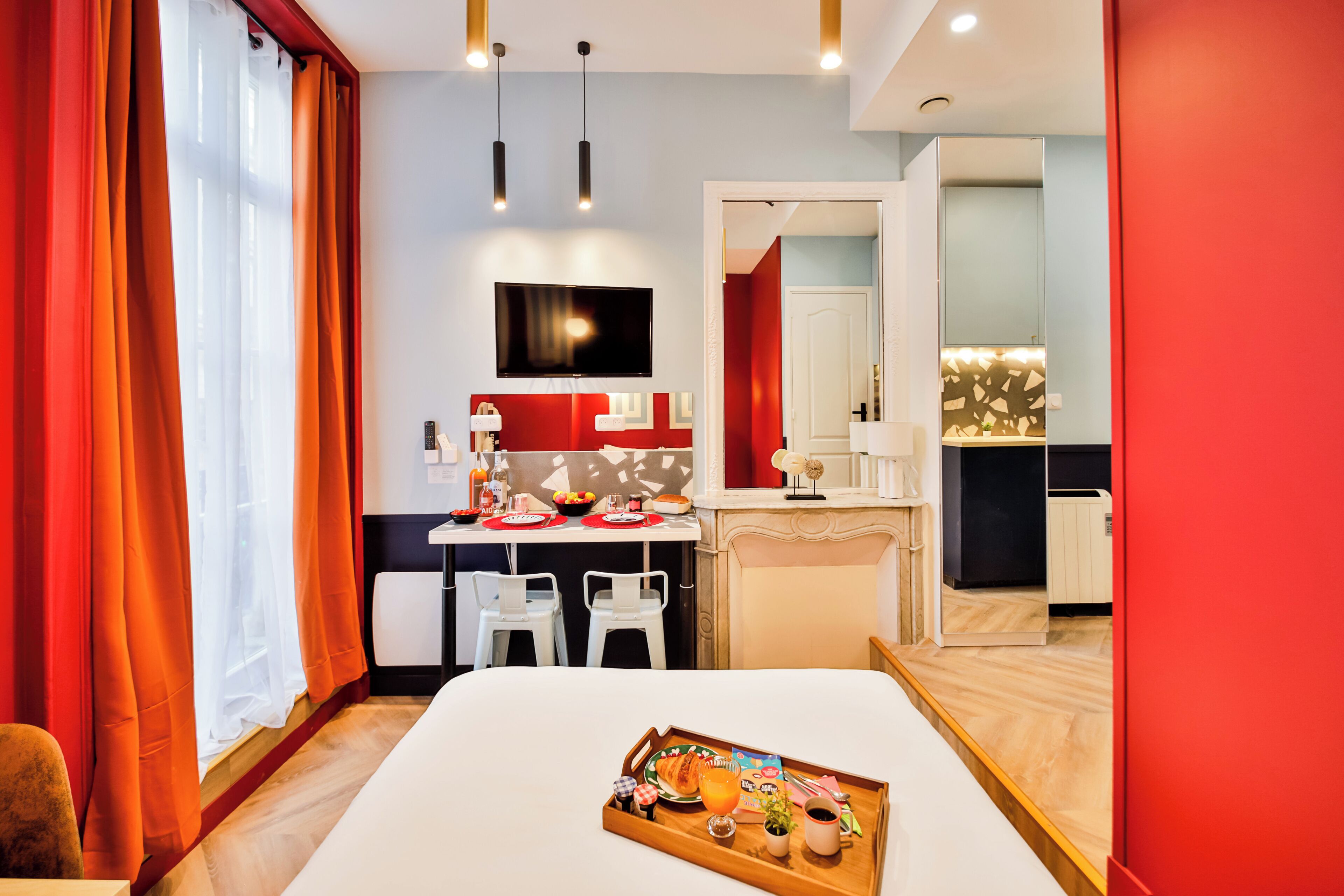 Une chambre d’hôtel moderne avec un coin repas, une télévision et un plateau de petit-déjeuner sur le lit.
