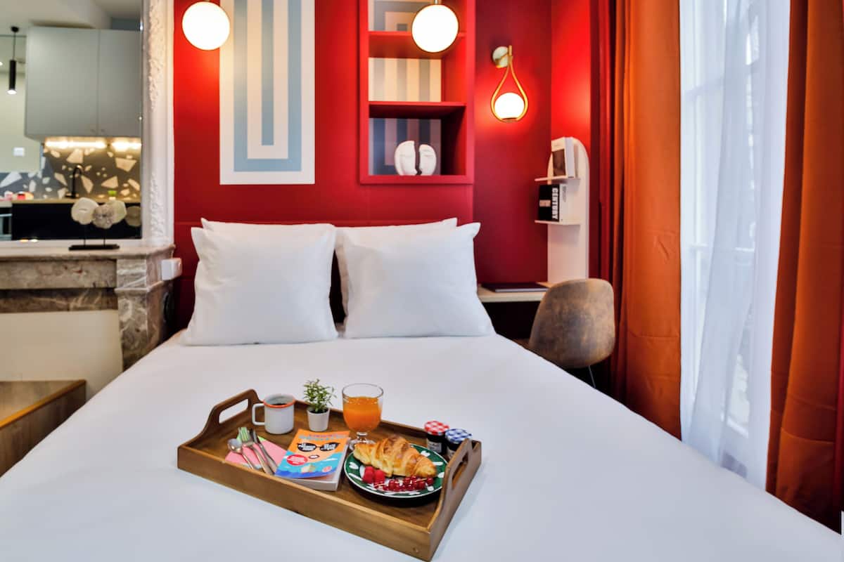Habitación de hotel con cama, bandeja de desayuno y pared roja con estante.