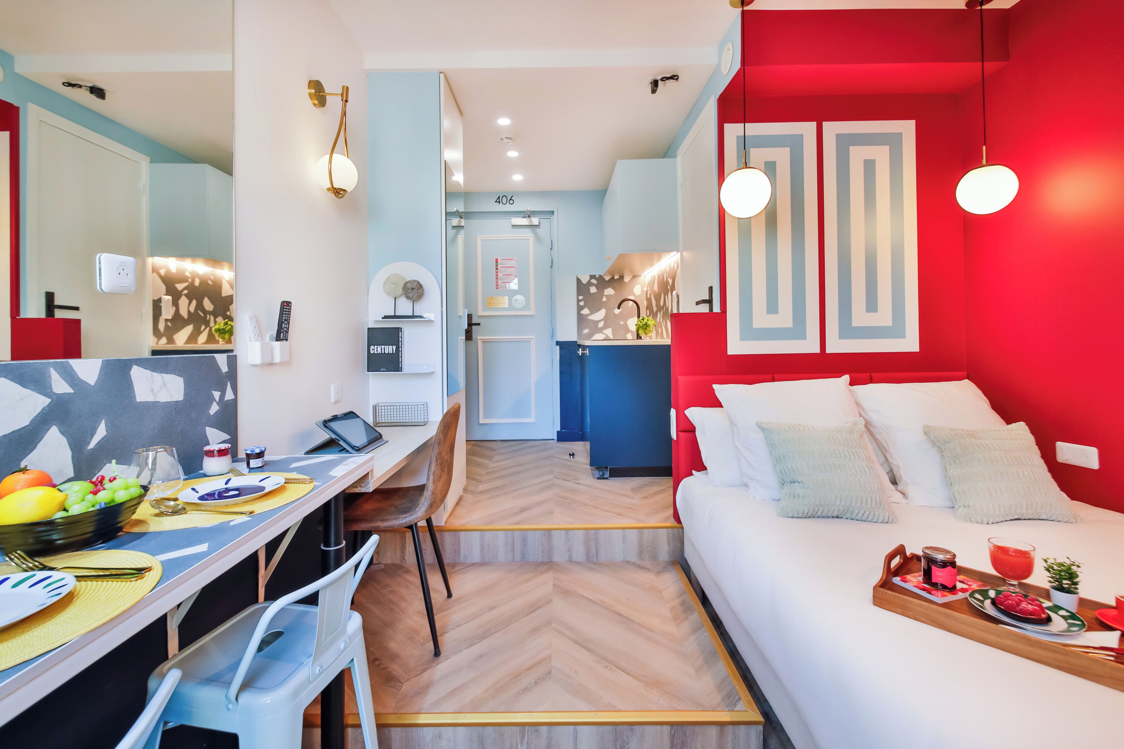 Une chambre d'hôtel compacte comprenant un coin repas, un lit avec un plateau de petit-déjeuner et un mur d'accent rouge.