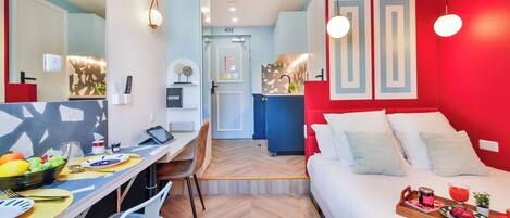 Une chambre d'hôtel compacte comprenant un coin repas, un lit avec un plateau de petit-déjeuner et un mur d'accent rouge.