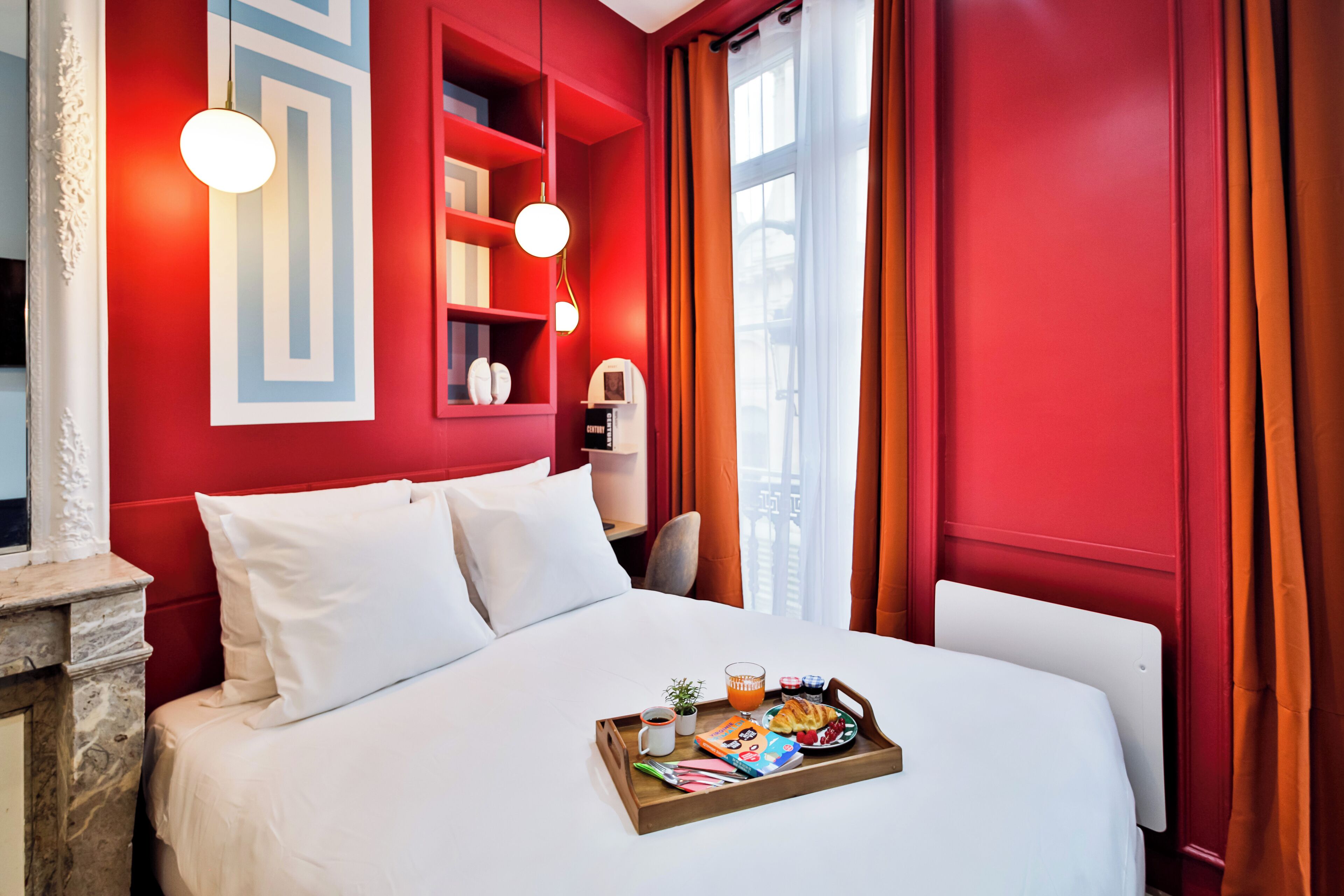 Habitación de hotel con una pared decorada en rojo, una cama blanca y una bandeja de desayuno sobre la cama.